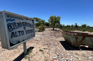 El cartel de bienvenida al barrio está rodeado de escombros y contenedores.